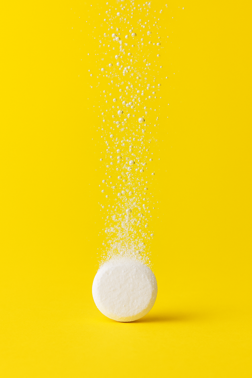 An effervescent tablet dissolving and fizzing in water against a bright yellow background