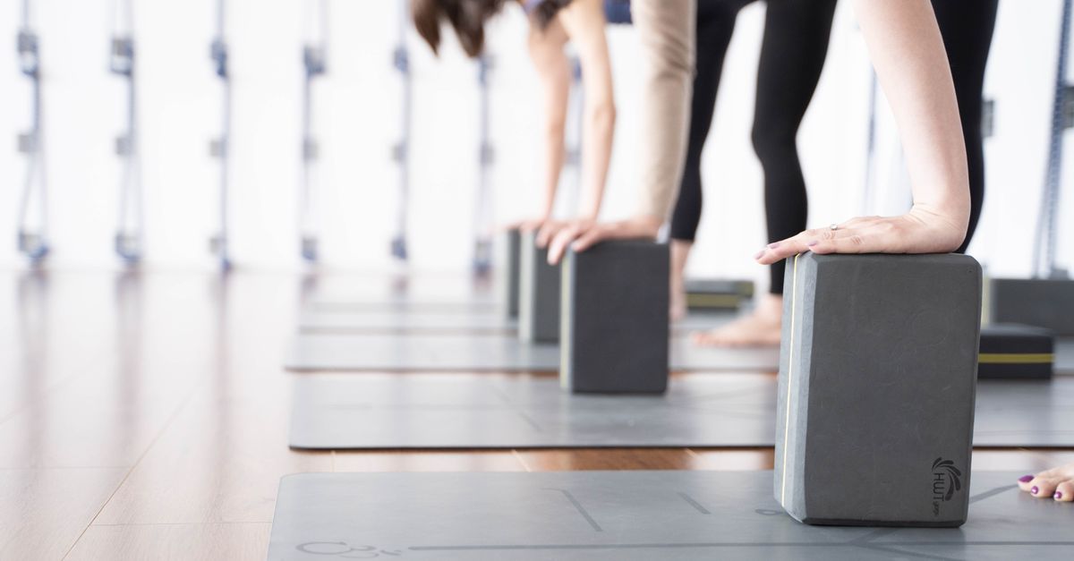 Hands reaching down onto foam yoga blocks in a studio, the prop that makes ardha chandrasana workable