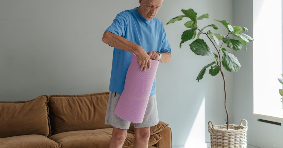 Older man unrolling an exercise mat at home to begin gentle belly fat exercises