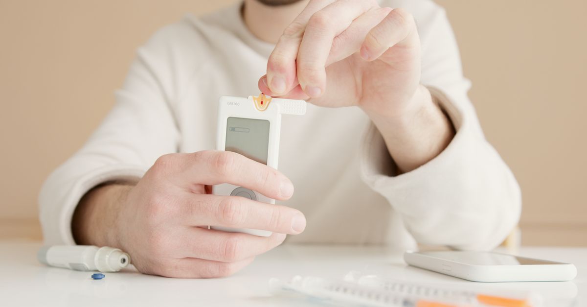 Person testing their blood sugar with a finger prick meter at a table, insulin handling in PCOS