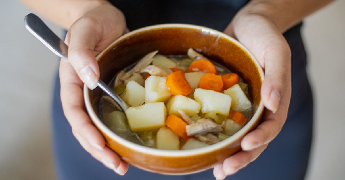 Hands holding a bowl of chunky vegetable soup, the way a bone broth base is best used