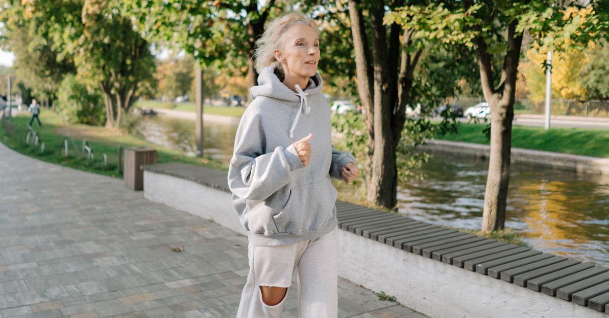 Older woman jogging along a tree lined canal path at a steady pace