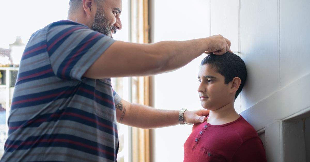 Father measuring his son's height against a wall, the growth measurement behind childhood obesity figures in India