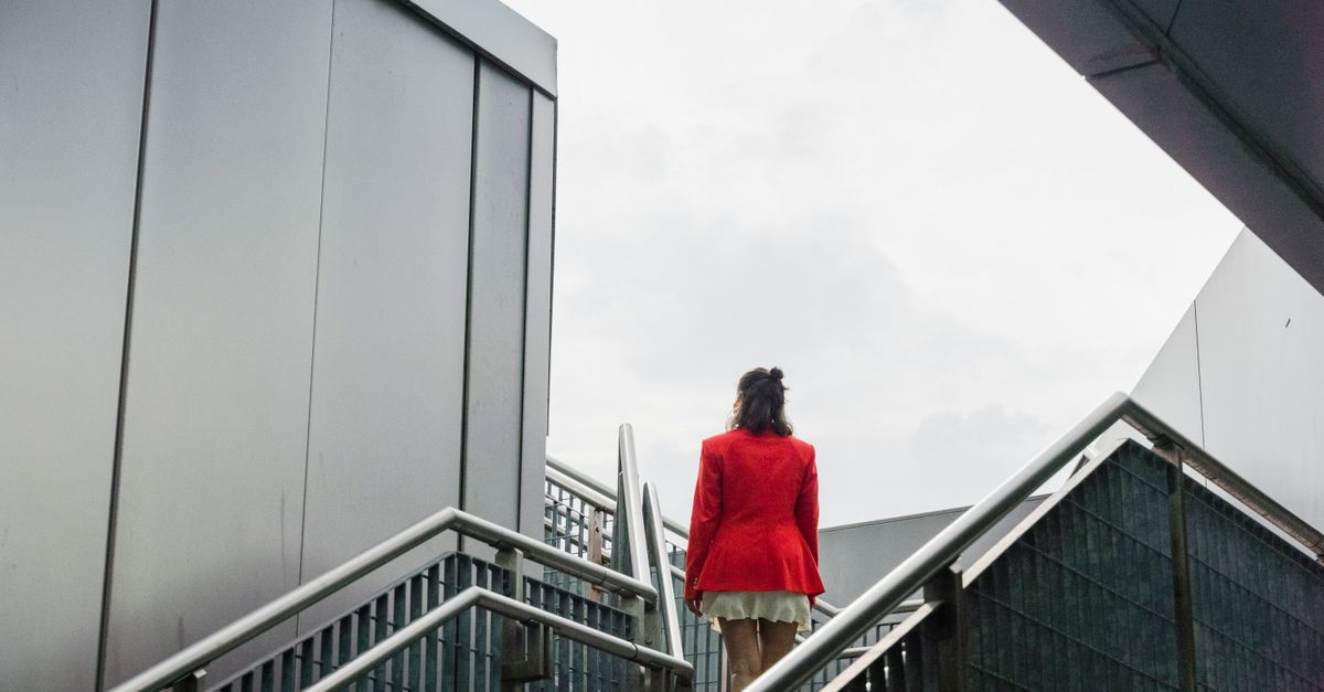 Woman in a red jacket climbing an outdoor city staircase, daily movement that shapes metabolism after 30