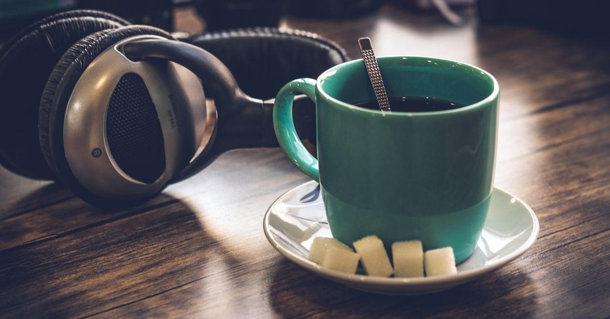 Green mug of black coffee beside sugar cubes on a saucer
