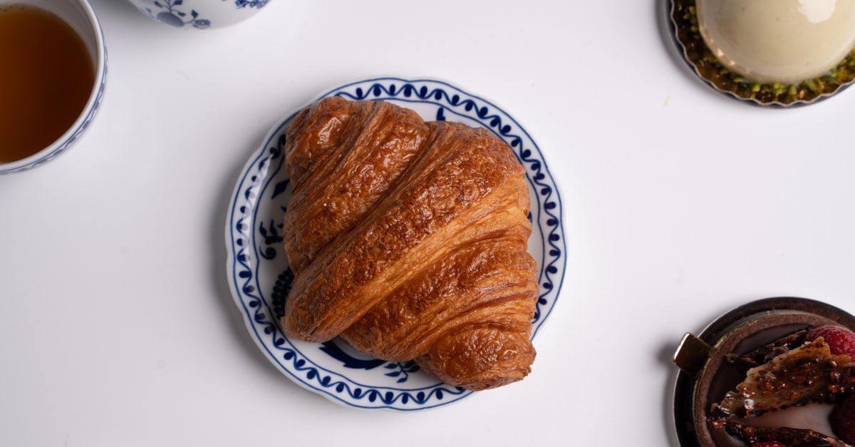 A buttery croissant on a small plate beside a cup of tea, a typical breakfast alongside grapefruit