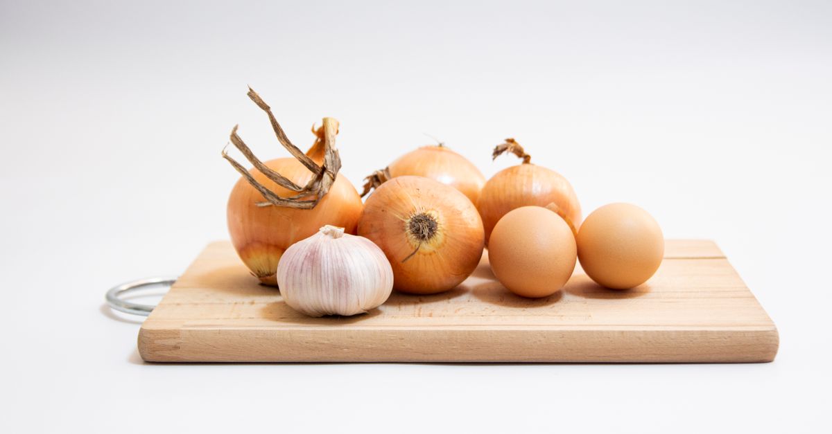 Brown eggs, onions and a bulb of garlic on a wooden board