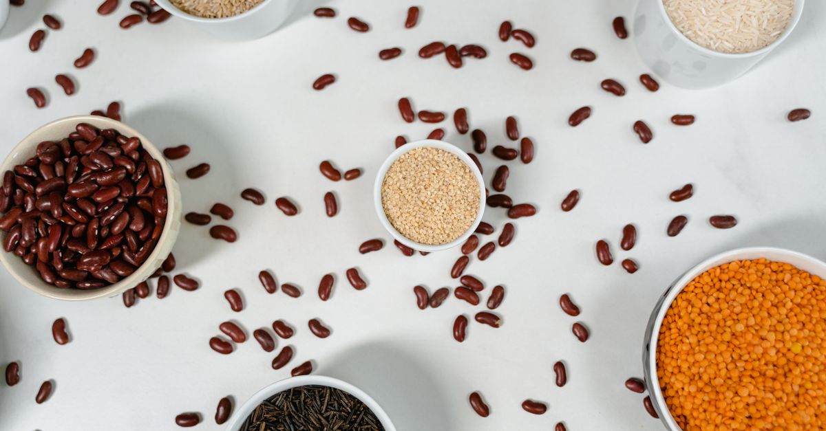 Small bowls of red lentils, kidney beans, quinoa and wild rice on a white surface