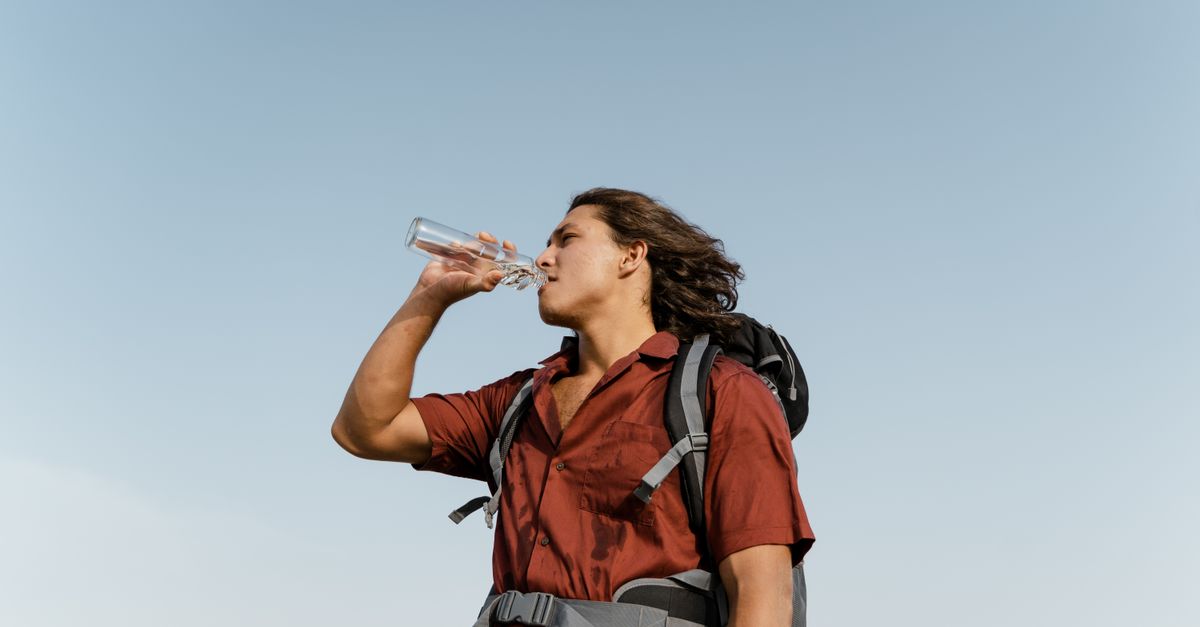 Person drinking from a water bottle outdoors under a bright sky, hydration on a summer walk