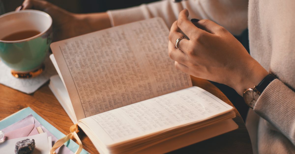 Woman writing in a handwritten journal beside a cup of coffee, tracking the triggers behind emotional eating