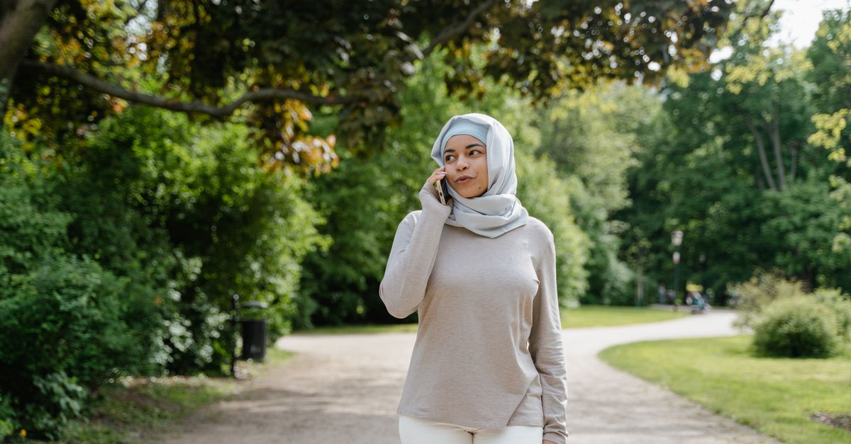 Woman in a hijab walking a green park path while talking on the phone