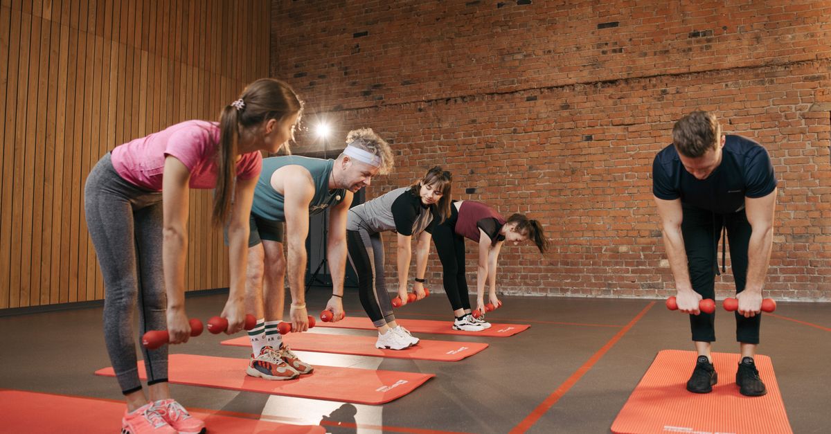 Mixed group fitness class training with dumbbells in a bright indoor studio, an after work workout time slot