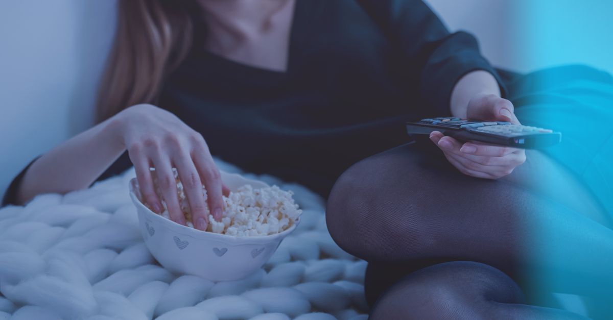 Hand reaching into a snack bowl by the light of a television, the evening cue behind sugar cravings