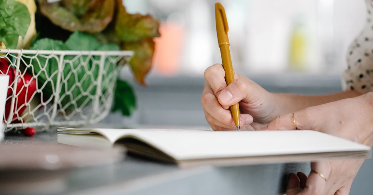 Hand writing in a food journal beside a basket of vegetables, the recall problem behind slow metabolism claims