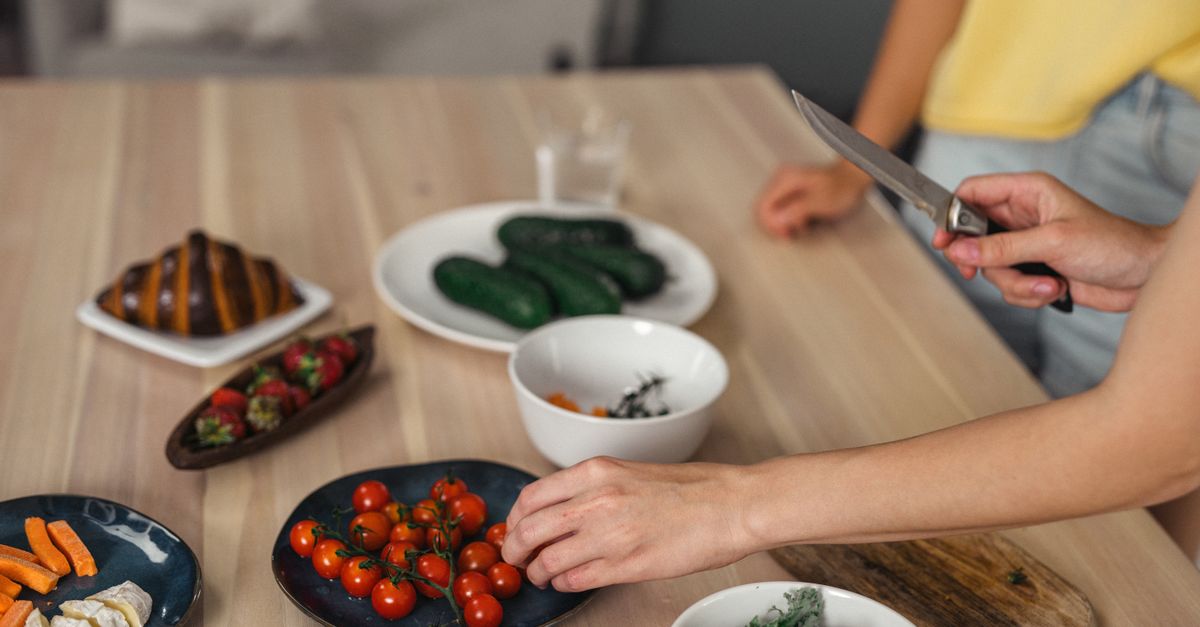 Hands slicing fresh vegetables at a wooden table, the lighter meals a detox drink takes credit for