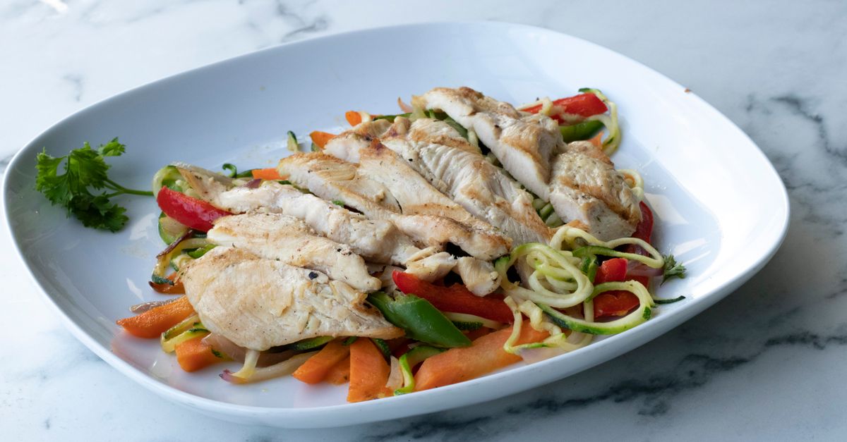 Sliced grilled chicken breast with vegetables on a white plate