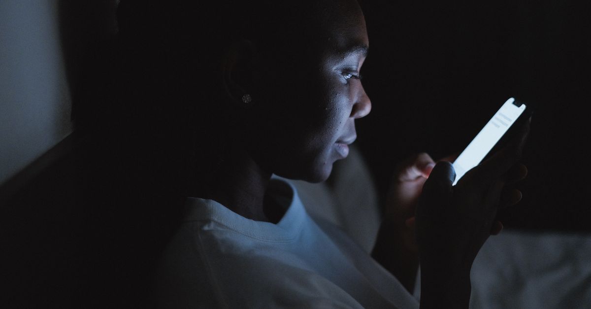 A man looking at a bright phone screen in a dark room at night