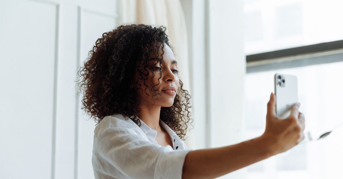 Woman photographing her face by a window in daylight to track face fat changes fairly