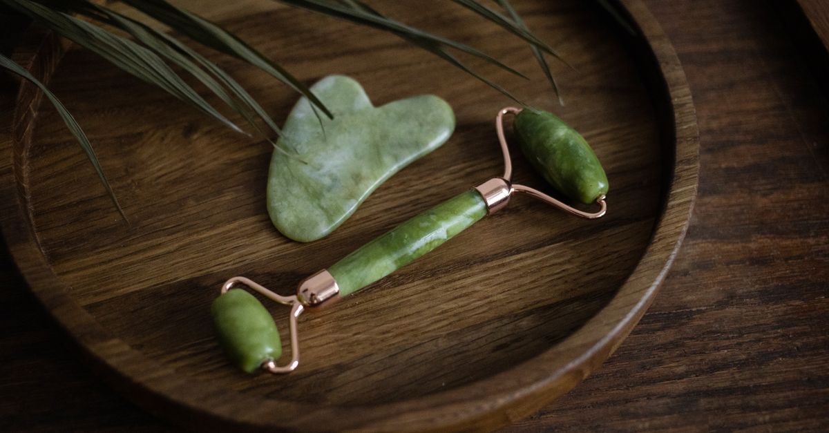 A jade facial roller and a gua sha stone on a wooden dish