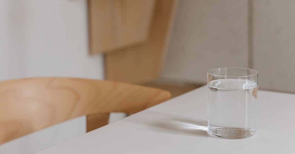 A plain glass of water on a wooden kitchen table, the main ingredient in any jeera water routine