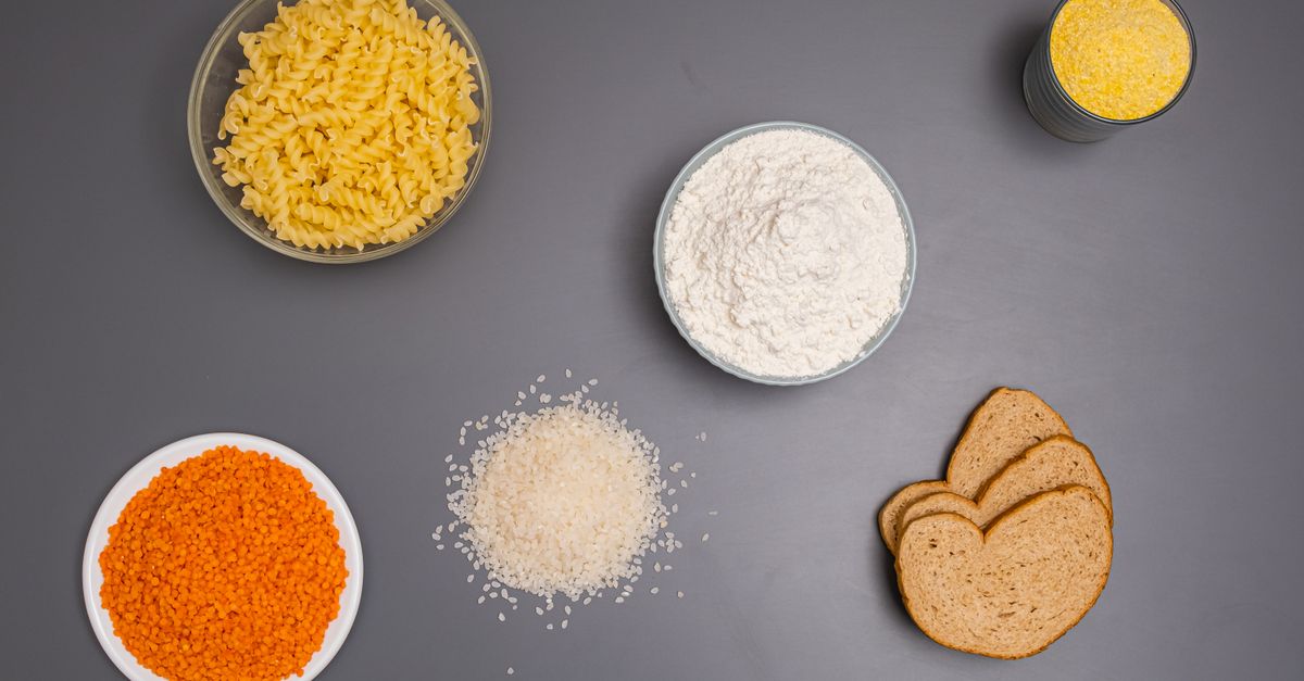 Pasta, rice, flour, lentils and bread laid out on a grey surface