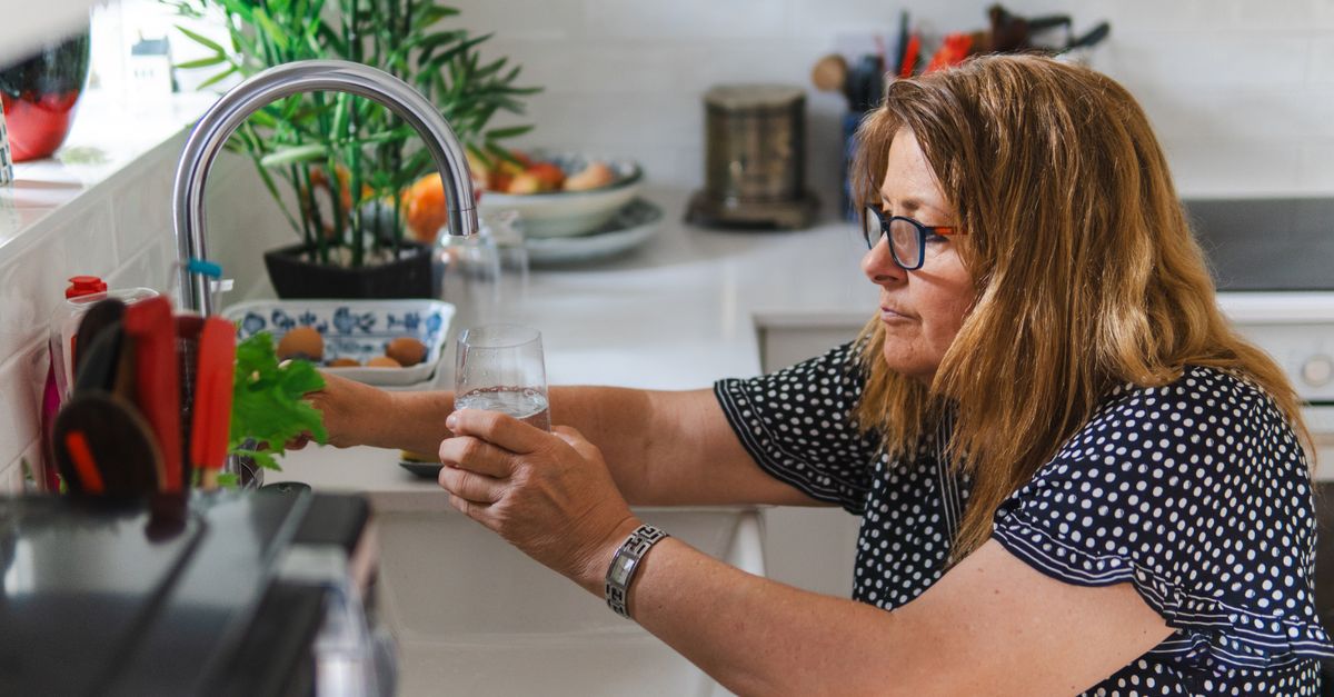 Woman filling a glass of water at a kitchen tap, hydration during the first week of a keto diet