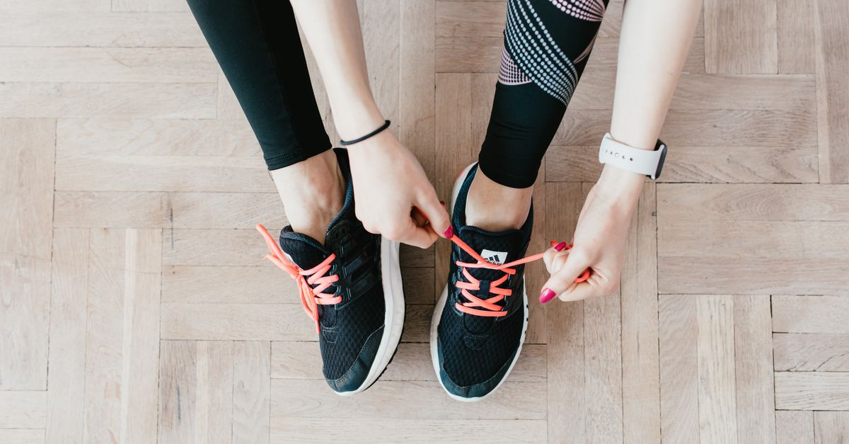 Overhead view of someone lacing black training shoes on a wooden floor at home