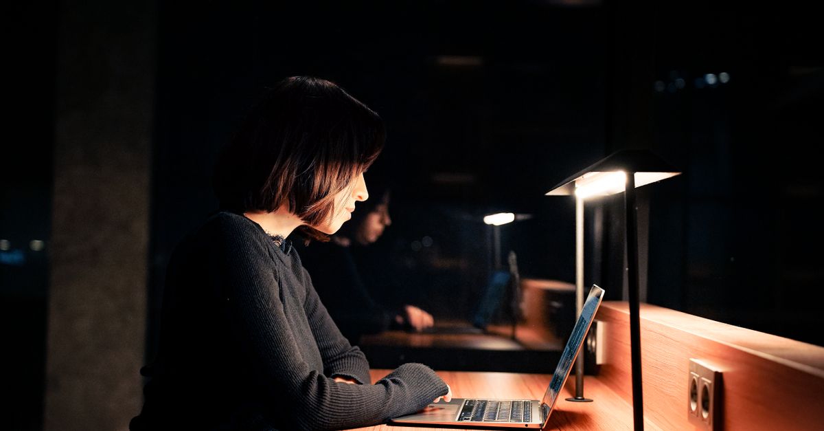 Woman working late at a desk lit only by her laptop and a small lamp