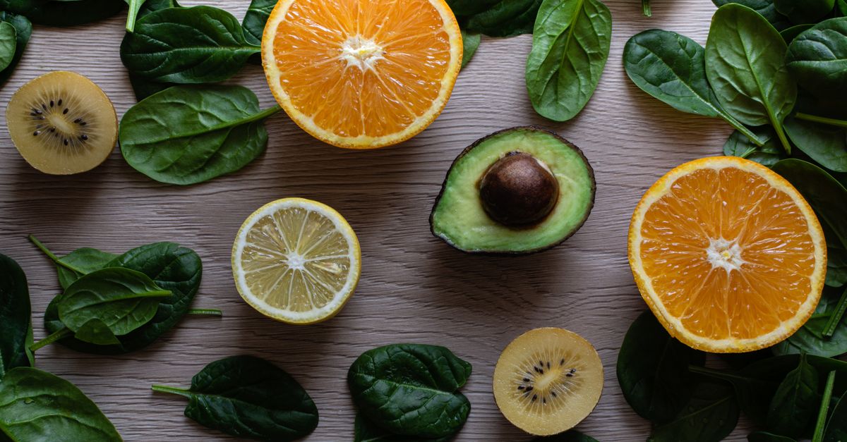 Sliced lemon, orange, kiwi and spinach laid out on a wooden board