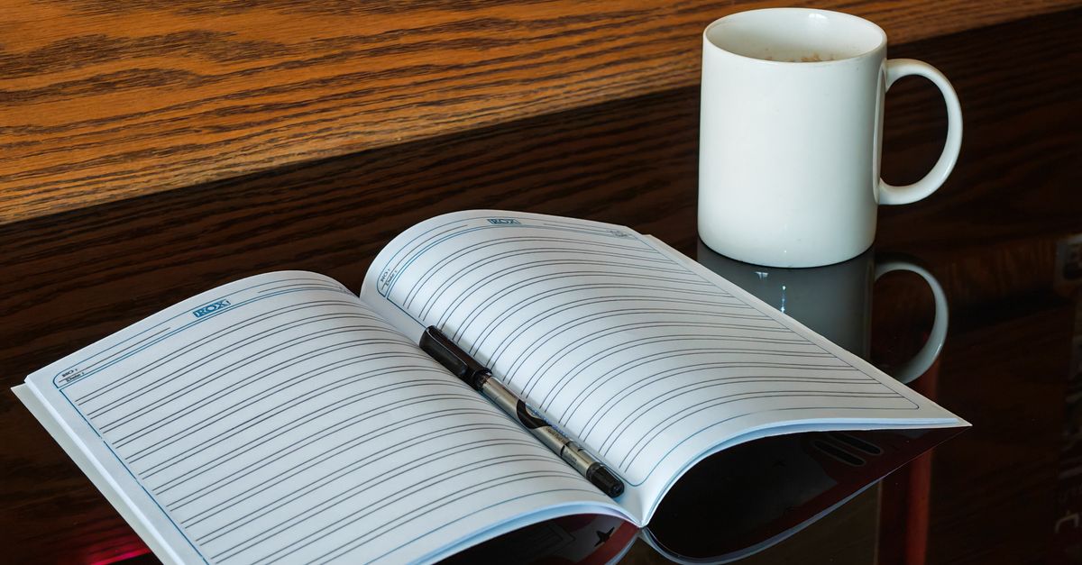 Open notebook and pen beside a mug, a training log for tracking muscle gain during fat loss