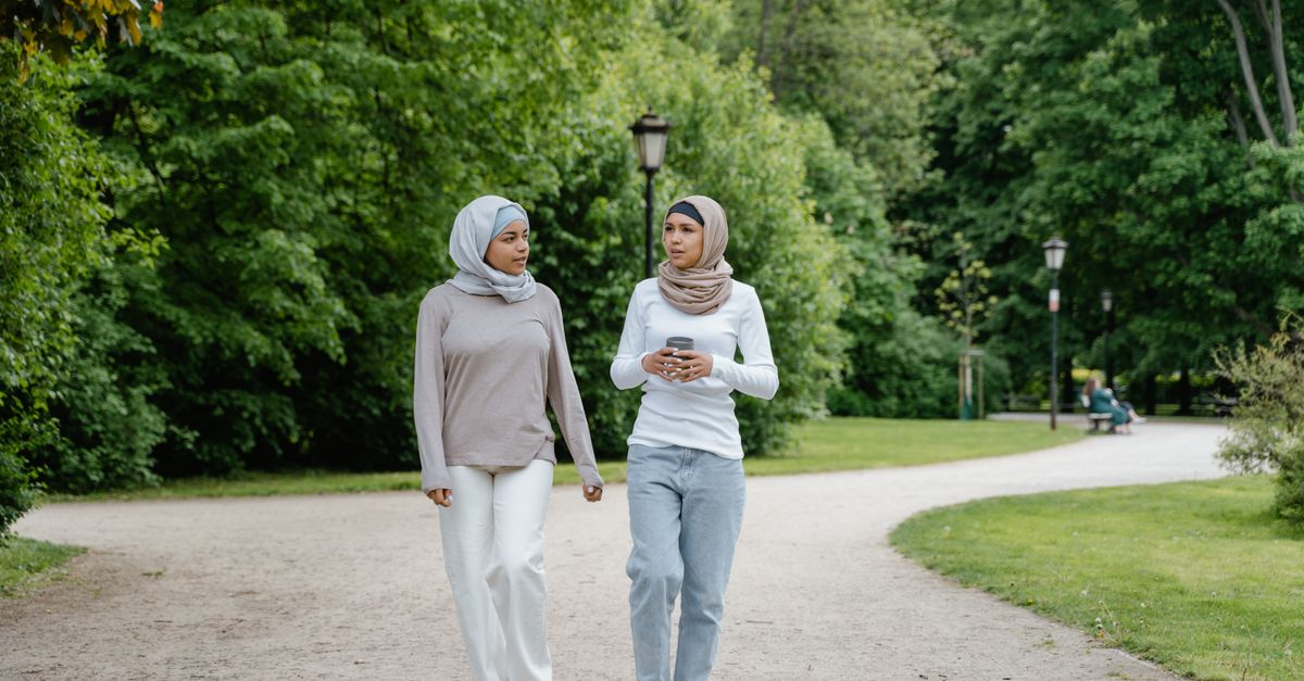Two women walking and talking along a green park path, everyday movement with PCOS