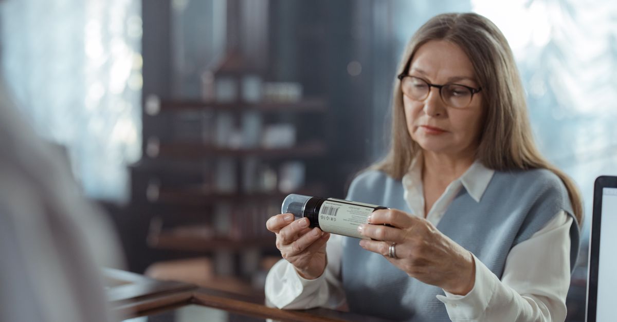 Woman in glasses reading the label on a supplement bottle, where the elemental magnesium figure is what counts