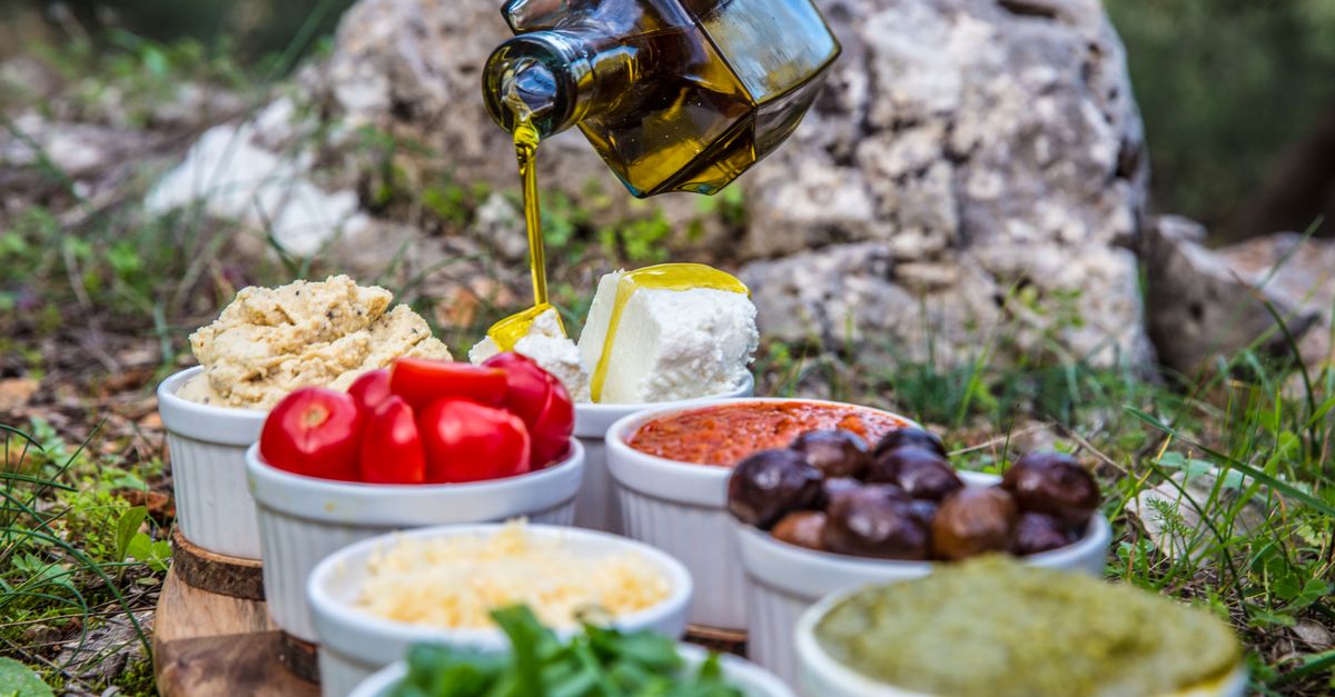 Olive oil poured over a Mediterranean spread of dips, olives and herbs