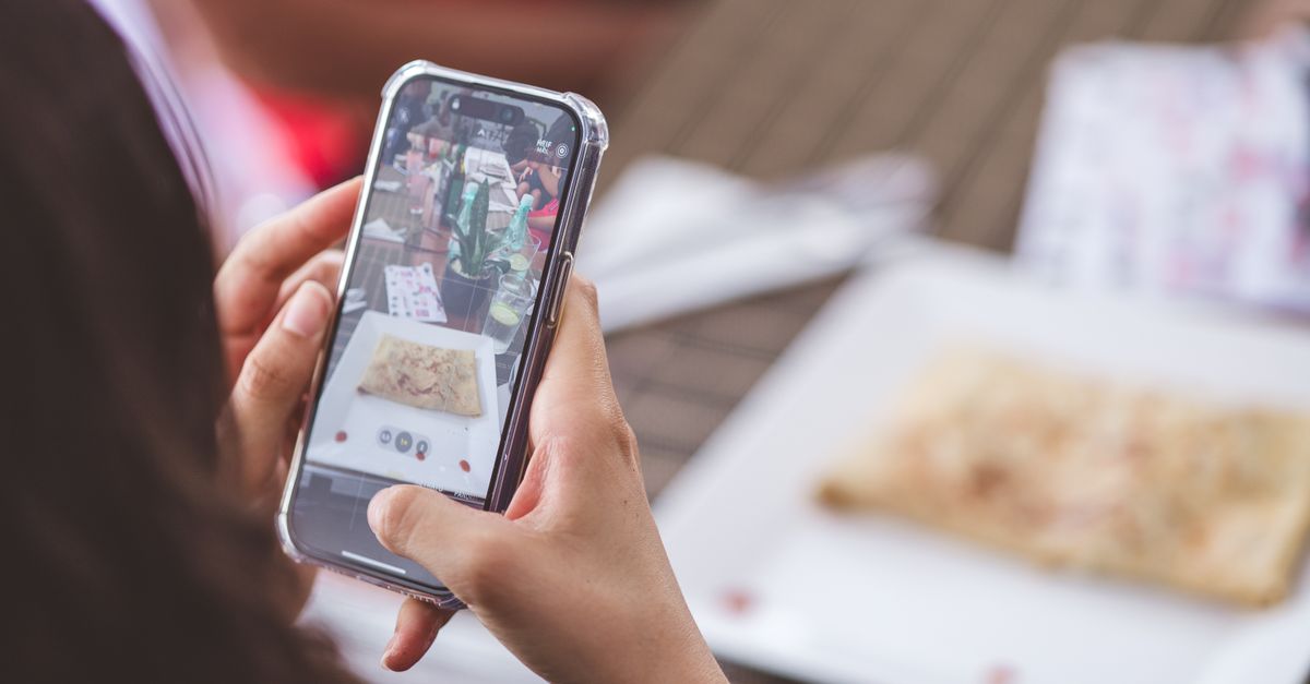 Hands holding a phone to photograph a plate of food on a table