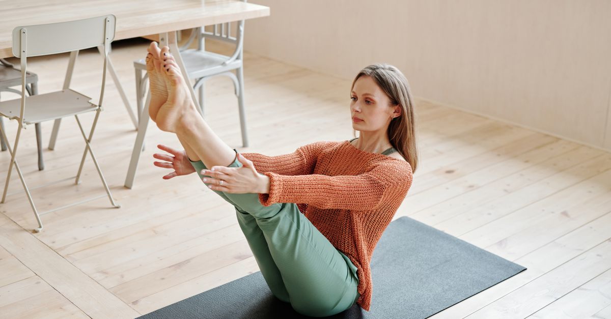 Woman balancing on an exercise mat in her living room during a mat Pilates session at home