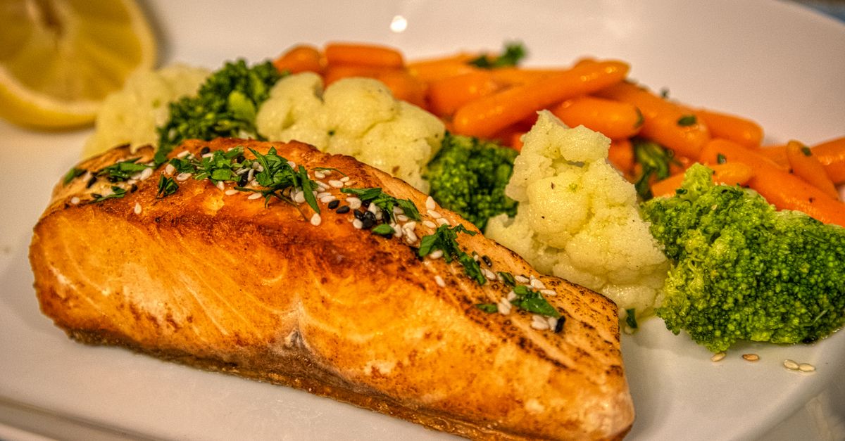Plate of grilled salmon served with steamed broccoli, cauliflower and carrots, broccoli as part of a filling meal