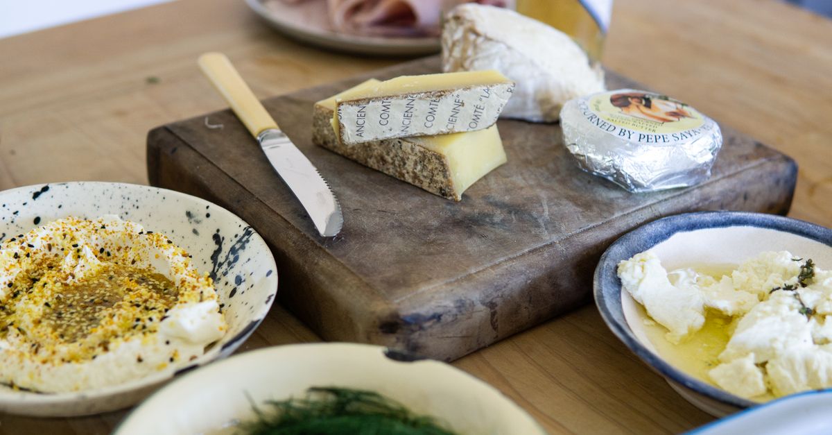 Cheese wedges and a knife on a wooden board beside bowls of dip, everyday sources of saturated fat