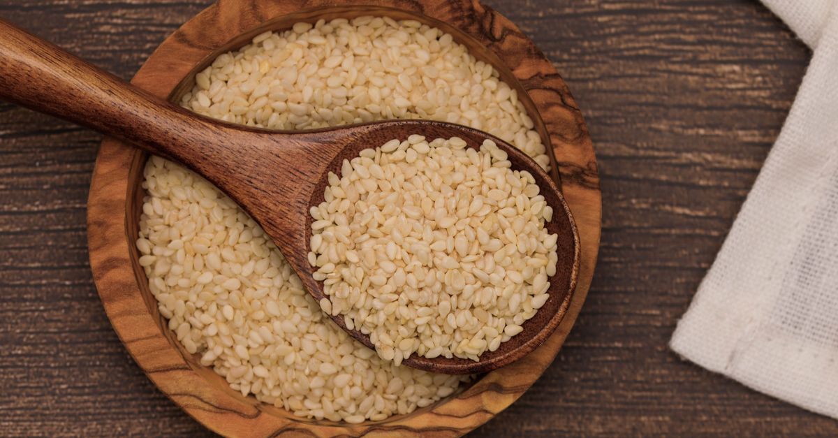 Whole unhulled sesame seeds in a wooden bowl and spoon, the form that carries the calcium