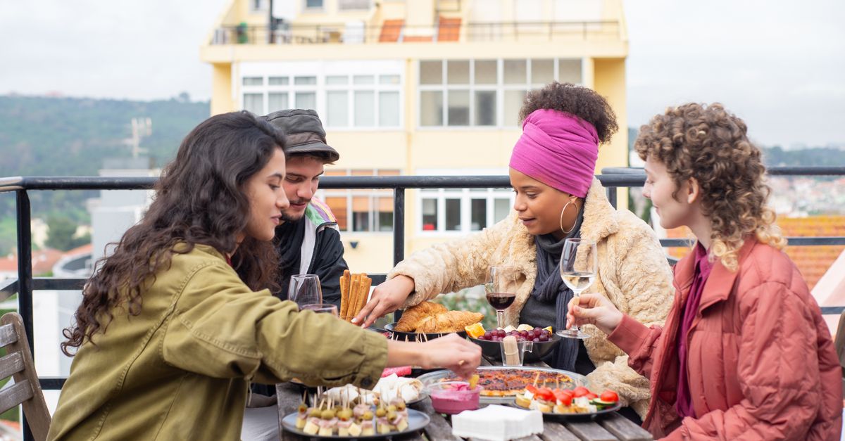 Friends passing dishes around a table on a sunny terrace