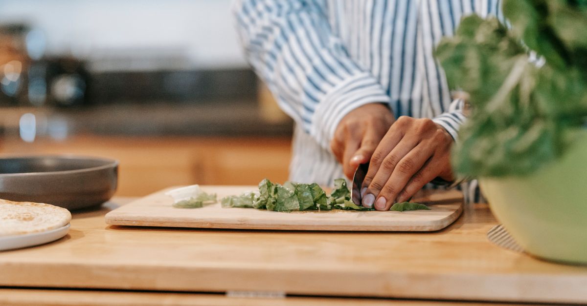 Person chopping fresh green vegetables on a wooden board, everyday eating that drives thigh fat loss