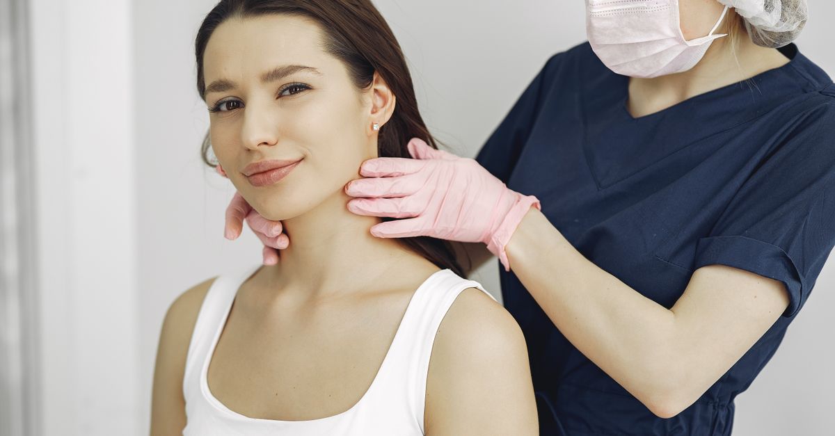 Clinician in scrubs examining a woman's neck, the thyroid check behind a hypothyroidism diagnosis