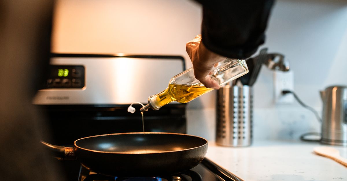 Olive oil poured from a bottle into a frying pan on a stove