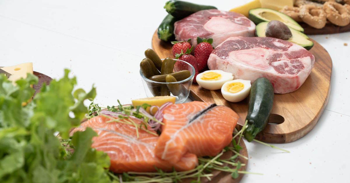Raw salmon fillets, sliced red meat, halved boiled eggs and salad leaves on a wooden board