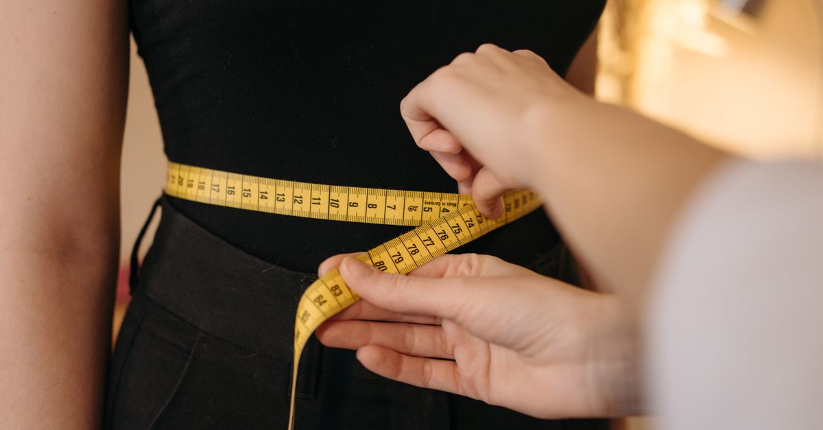 Hands measuring a waist with a tape measure, because waist size tracks the visceral fat that drives chronic inflammation