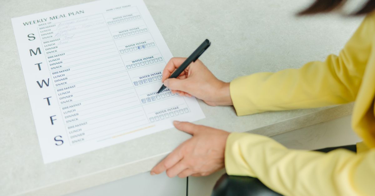Hand filling in a weekly meal plan sheet at a table