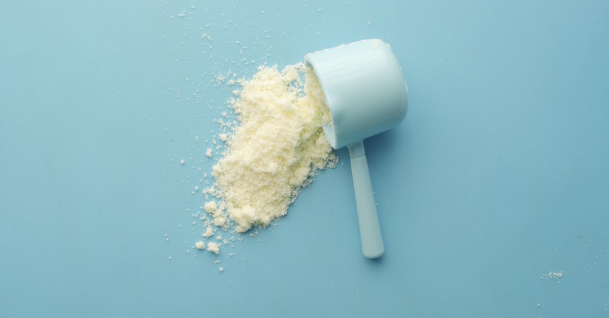 Scoop of white whey protein powder spilled on a plain blue surface