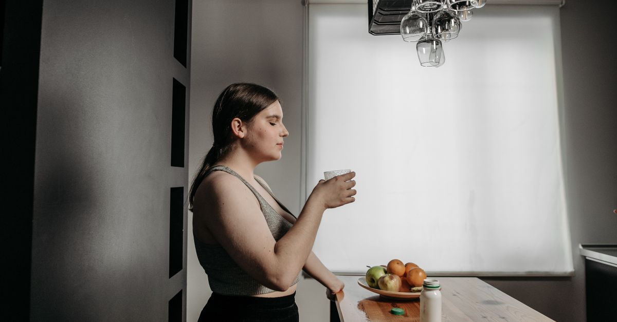 Woman holding a glass of water by a kitchen window, plain water beside tamarind and lemon